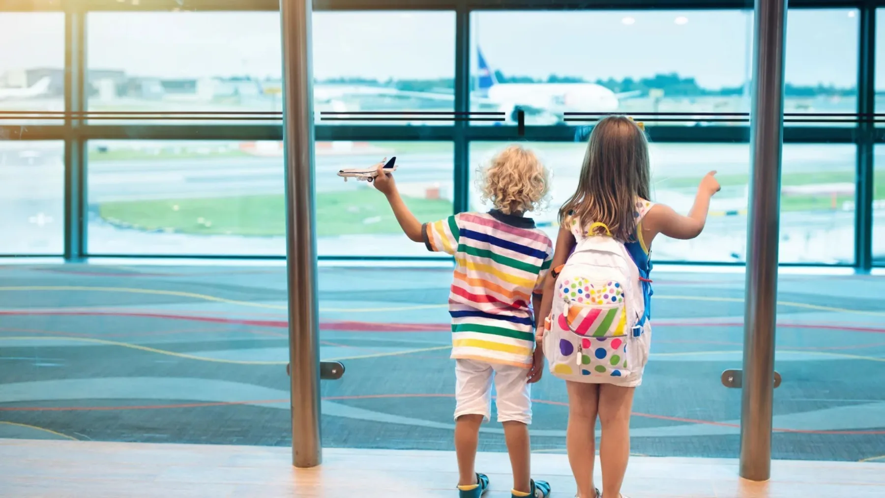 Duas crianças com mochilas observam um avião no aeroporto. Documentos e autorização de viagem para menores de idade que vão à Argentina.