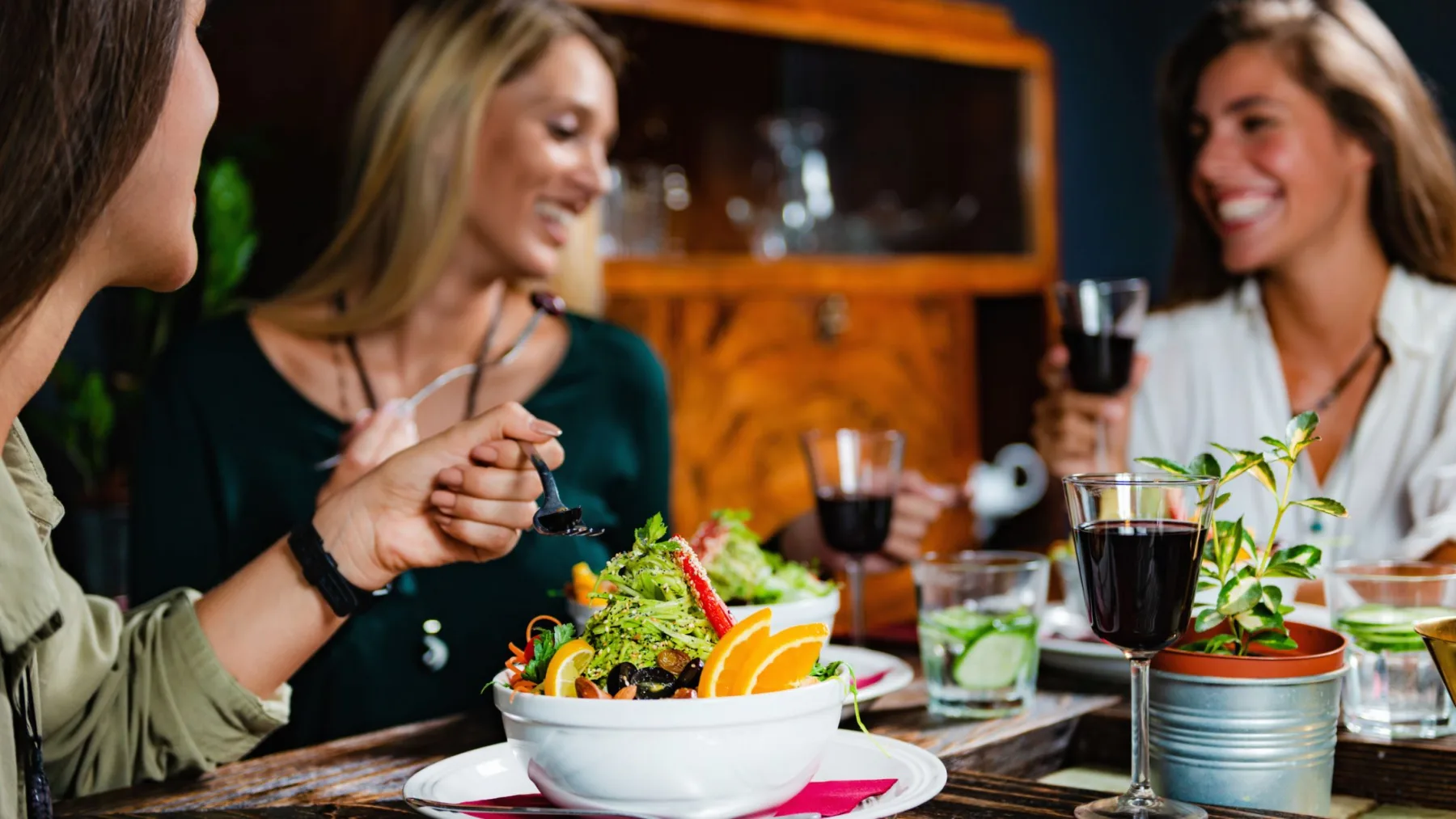 Mulheres reunidas em um restaurante, compartilhando pratos vegetarianos, saladas e bebidas durante uma refeição.